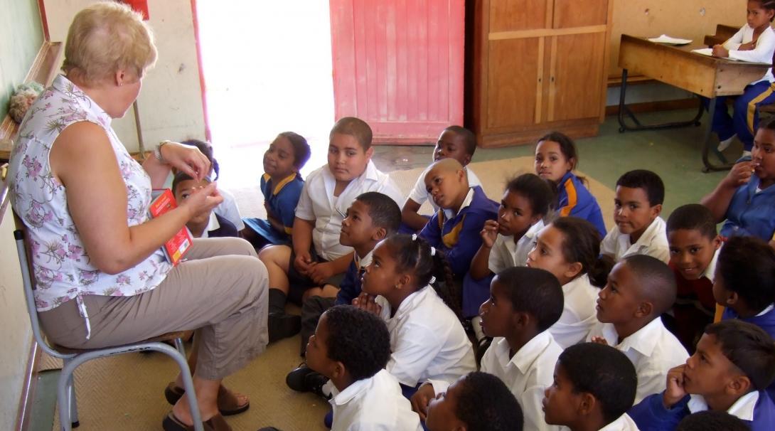 Voluntaria senior enseñando inglés en Sudáfrica. Niños escuchan la clase de inglés de voluntaria de educación.